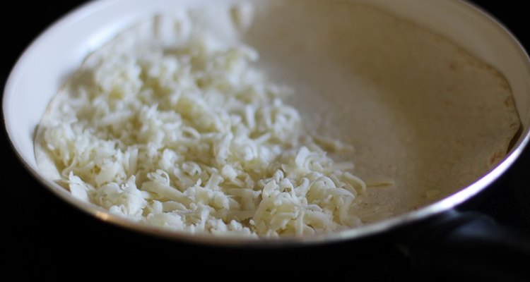 Half of a flour tortilla covered with cheese in a skillet.