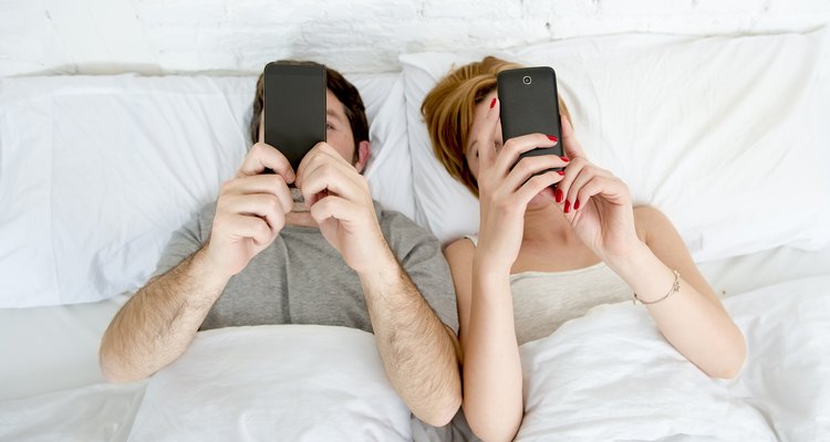 Couple laying in bed looking at their smart phones.