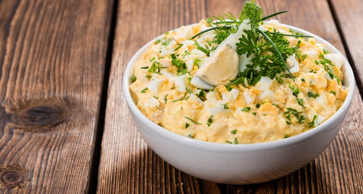 A bowl of egg salad topped with a boiled egg slice and parsley