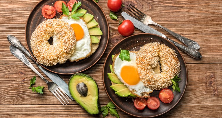 Bagel with avocado and egg on the wooden background.