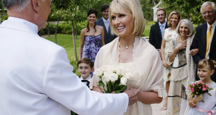 Bride and groom smiling with wedding guests in background