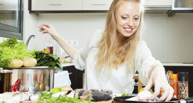 Happy woman putting fish in flour into frying pan