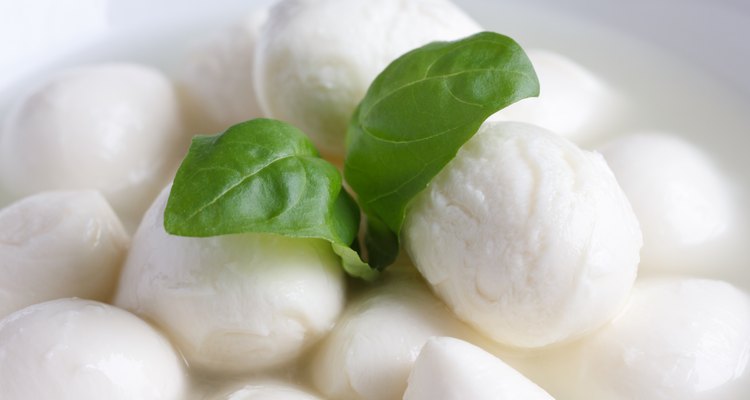 Small mozzarella balls in a white dish with liquid.