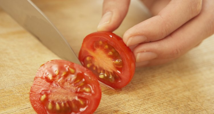 Woman cutting cherry tomato, close up