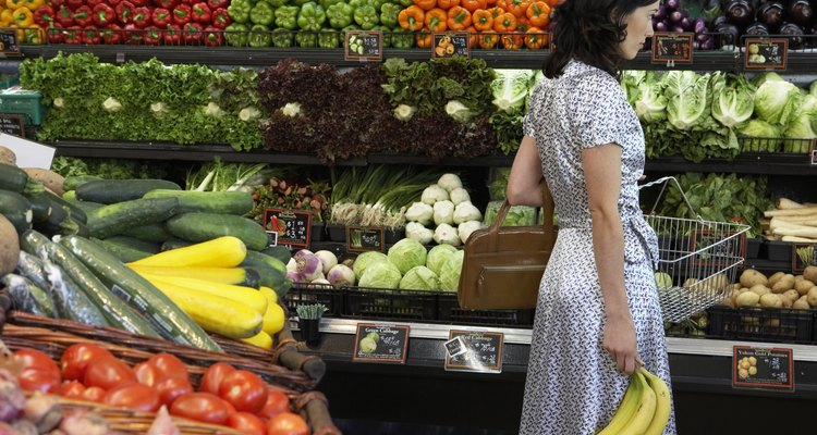 Woman holding bananas in produce aisle of supermarket, side view
