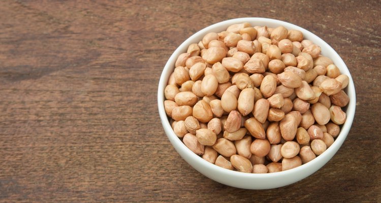 Raw peanuts in white bowl on wooden table.