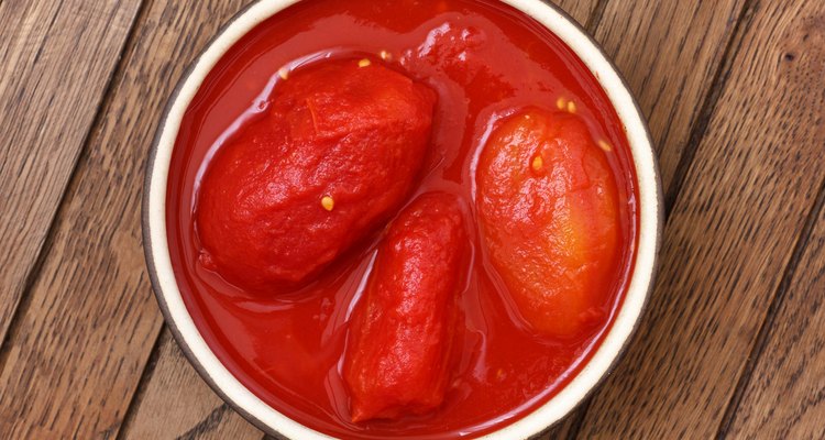 Whole canned tomatoes in pottery dish from above on wood.