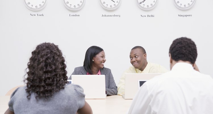Business men and woman using laptops in office with clocks on wall